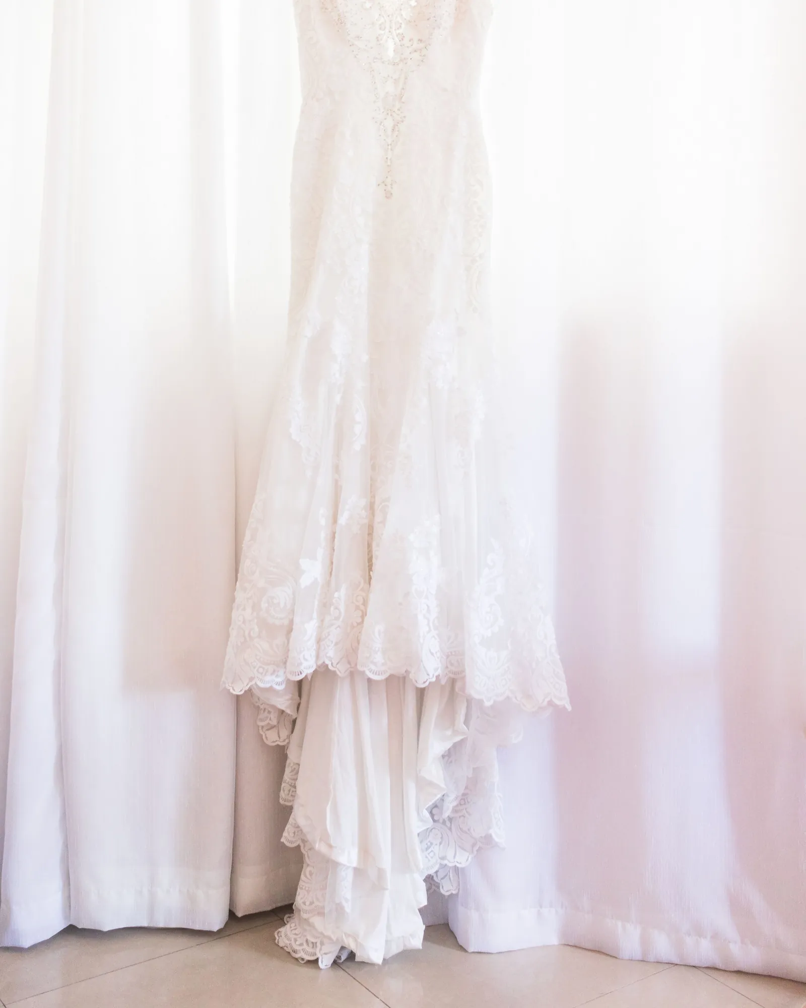 A lace occasion dress hanging in bright window light
